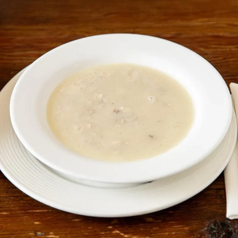 Creamy soup with textured pieces in white bowl on wooden table.