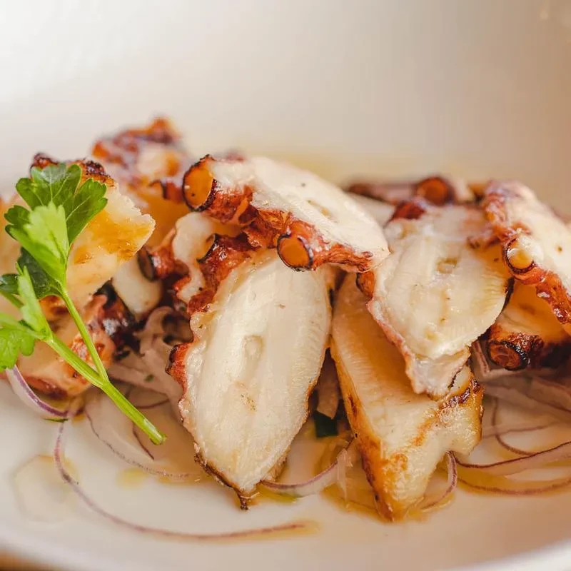 Sliced, grilled octopus with red onion, olive oil, and parsley.