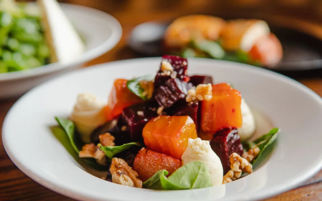 Colorful beet, walnut, green leaf salad with creamy dollops on white plate.