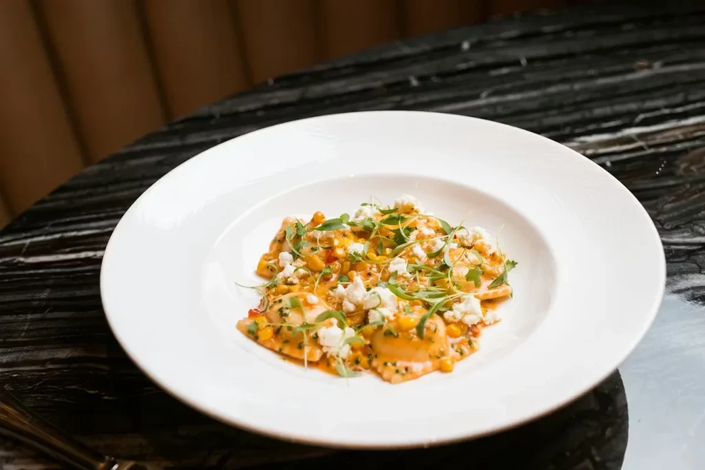 Pasta with orange sauce, crumbled cheese, corn, and microgreens.