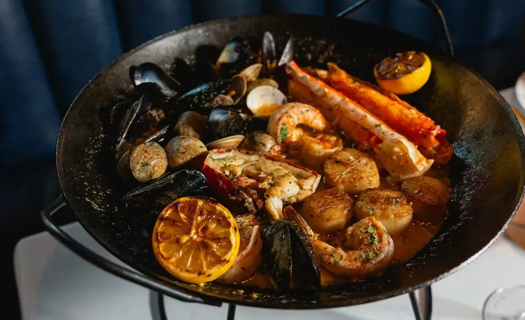 Rustic pan of cooked shellfish and crustaceans, garnished with lemon.