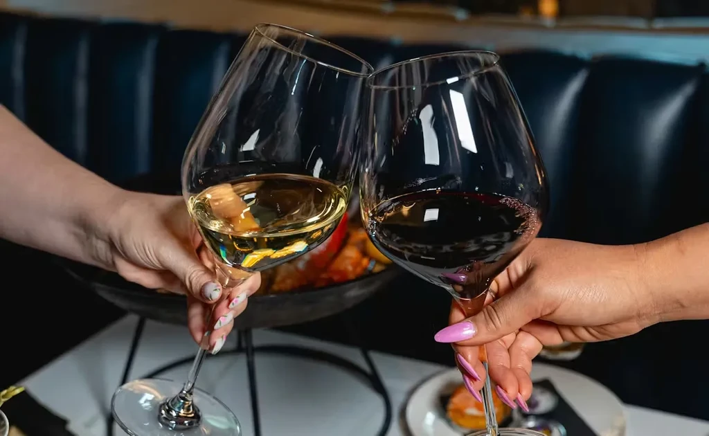 Different hands toast white and red wine glasses in a restaurant.