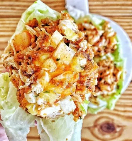 Two chicken and pineapple lettuce wraps with sauce on wood.