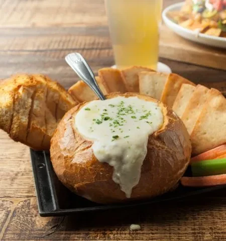 Crusty bread bowl with creamy dip, assorted breads, and vegetables.