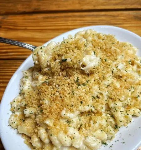 Fork scooping creamy macaroni and cheese topped with breadcrumbs and herbs.