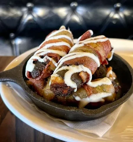 Golden-brown bacon-wrapped appetizers with creamy sauce in a skillet.