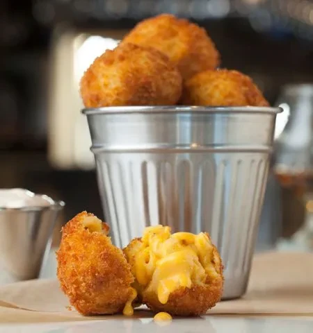 Golden-brown deep-fried mac and cheese balls, one broken, showing gooey filling.