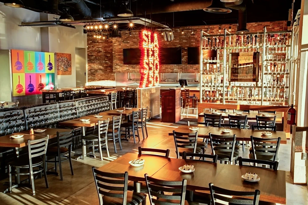 Empty industrial restaurant interior with booths, bar, neon sign, and burger art.