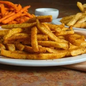 Close-up: seasoned french fries, other fries, and dipping sauce.