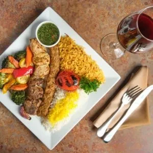 Kebabs, two rices, and roasted vegetables on a white plate.