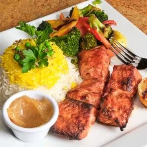 Well-plated grilled salmon, rice, roasted vegetables, creamy sauce, and lemon.