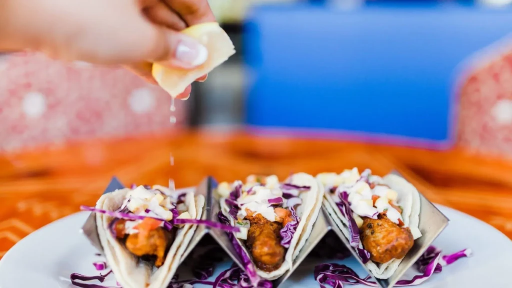 Hand squeezing lemon over three fish tacos with cabbage and tomatoes.