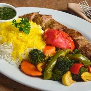 Middle Eastern dish: saffron rice, grilled meat skewer, roasted vegetables, dipping sauce.