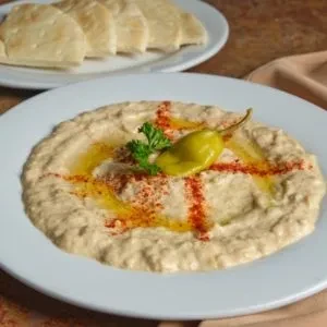 Top-down view of garnished hummus or baba ghanoush with pita bread.