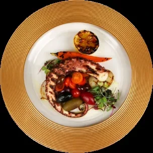 Overhead view of grilled octopus, microgreens, and vegetables on a gold-rimmed plate.