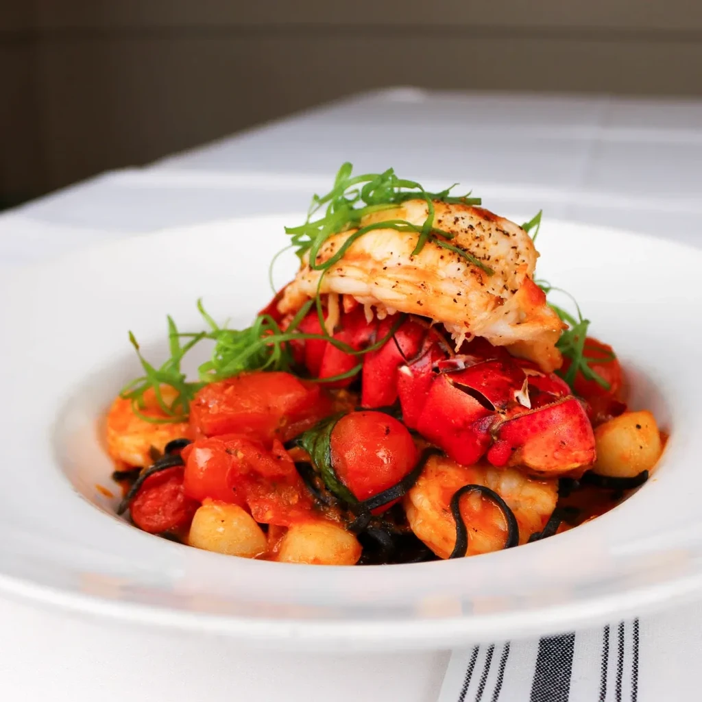 Plated squid ink pasta with lobster, cherry tomatoes, and fresh herbs.
