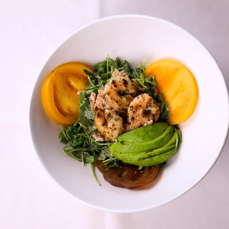 Grilled shrimp salad with avocado, colorful tomatoes, and greens.