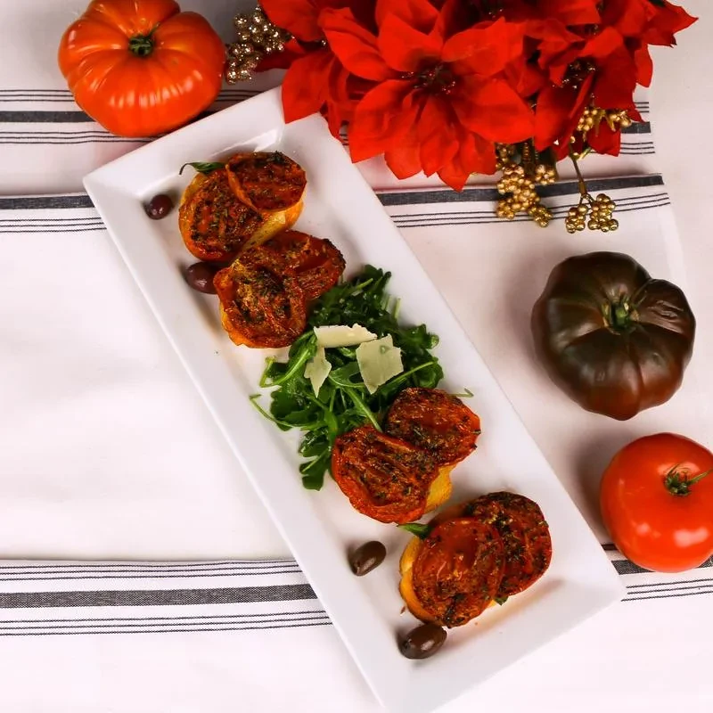 Plated bruschetta with roasted tomatoes, arugula, Parmesan, olives, and heirloom tomatoes.