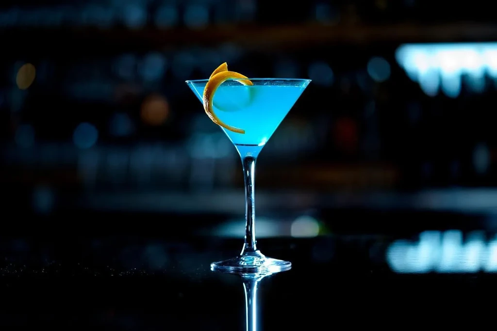 Vibrant blue cocktail in martini glass with orange peel garnish.