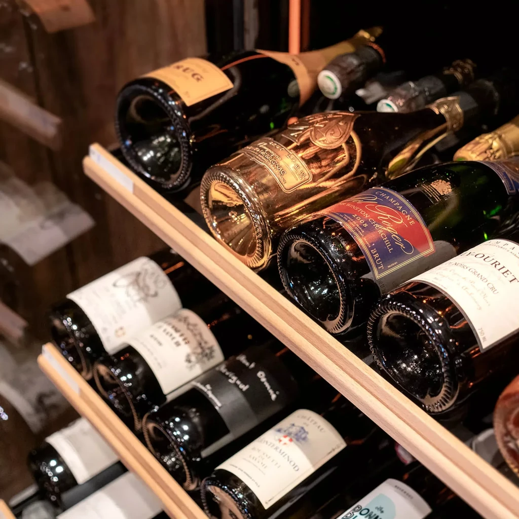 Golden-labeled champagne and various wine bottles on wooden shelves.