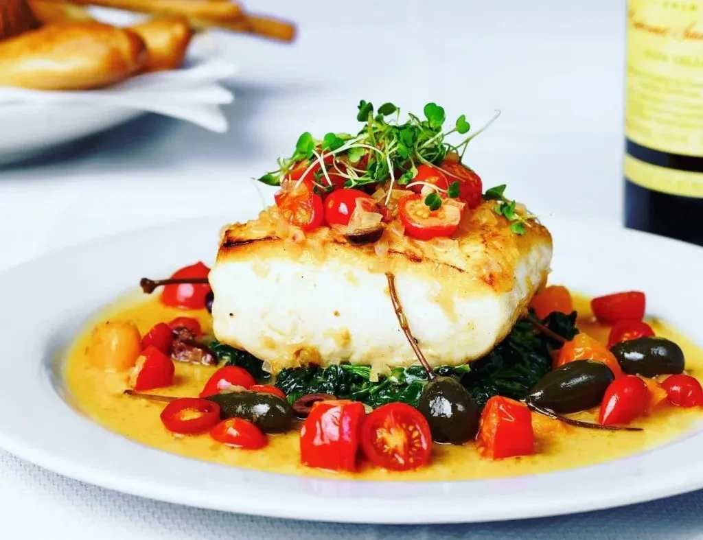 Seared white fish with tomato salsa, greens, and yellow sauce.