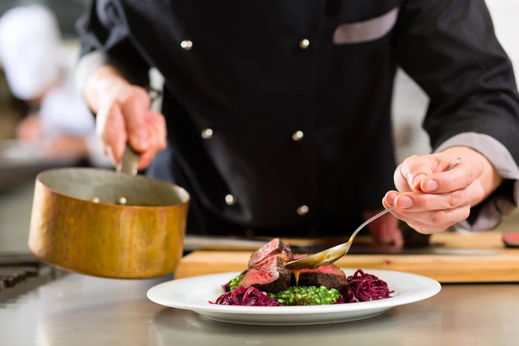 Chef in black jacket meticulously plating a vibrant, elegant dish.