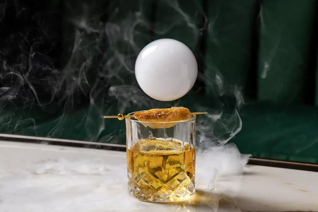 Faceted cocktail glass with spherical smoke bubble and tendrils.
