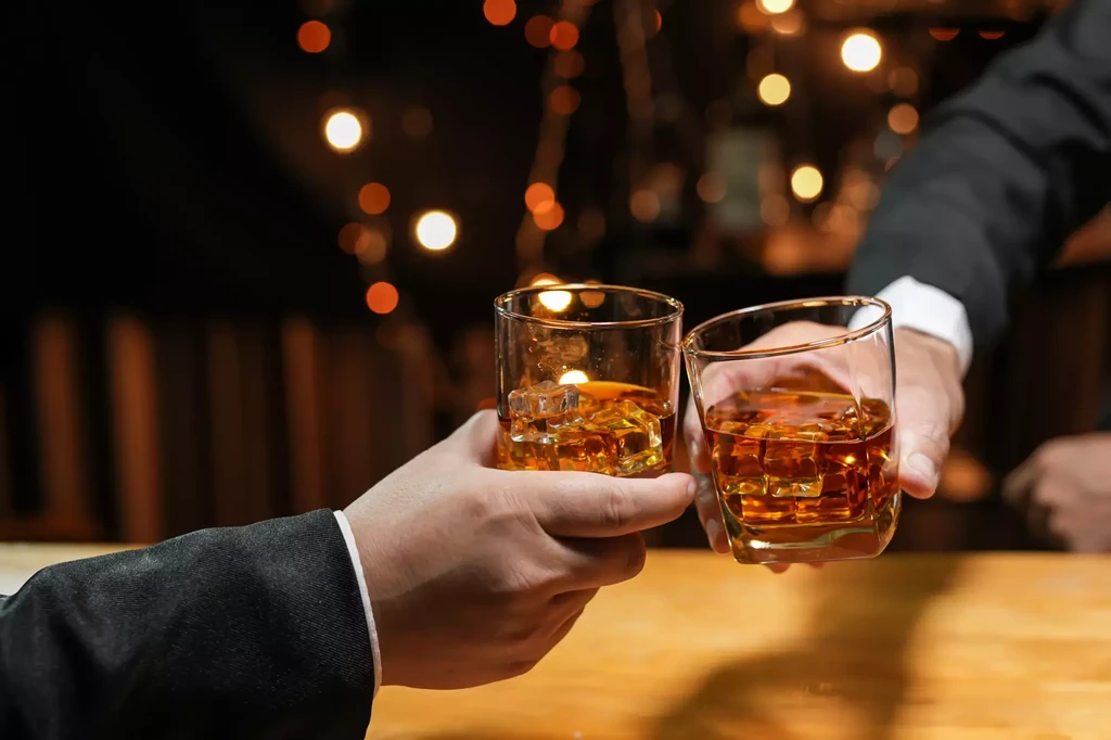 Two formal hands toasting glasses of whiskey with ice.