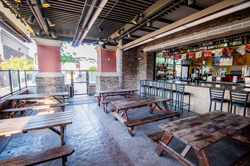 Open-air restaurant patio with wooden picnic tables and a stocked bar.