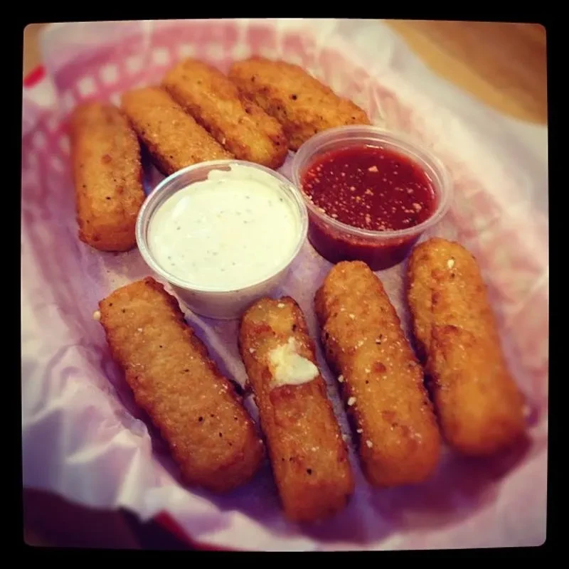 Golden-brown fried mozzarella sticks in a checkered basket with two sauces.