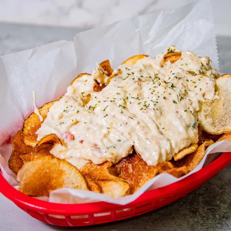 Golden potato chips in red basket, topped with creamy sauce and herbs.