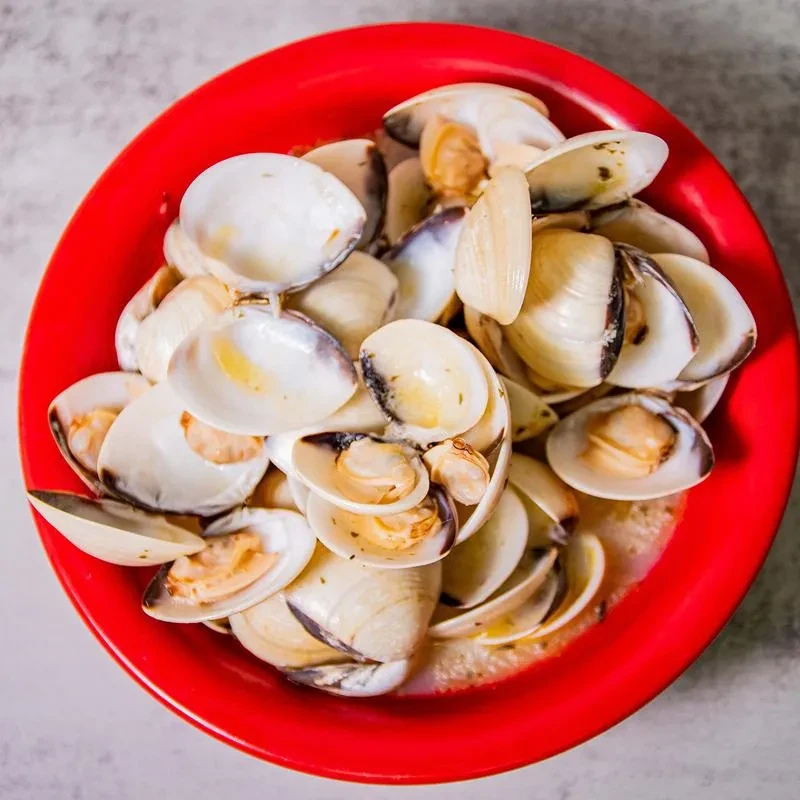 Steamed clams in a vibrant red bowl with creamy broth.