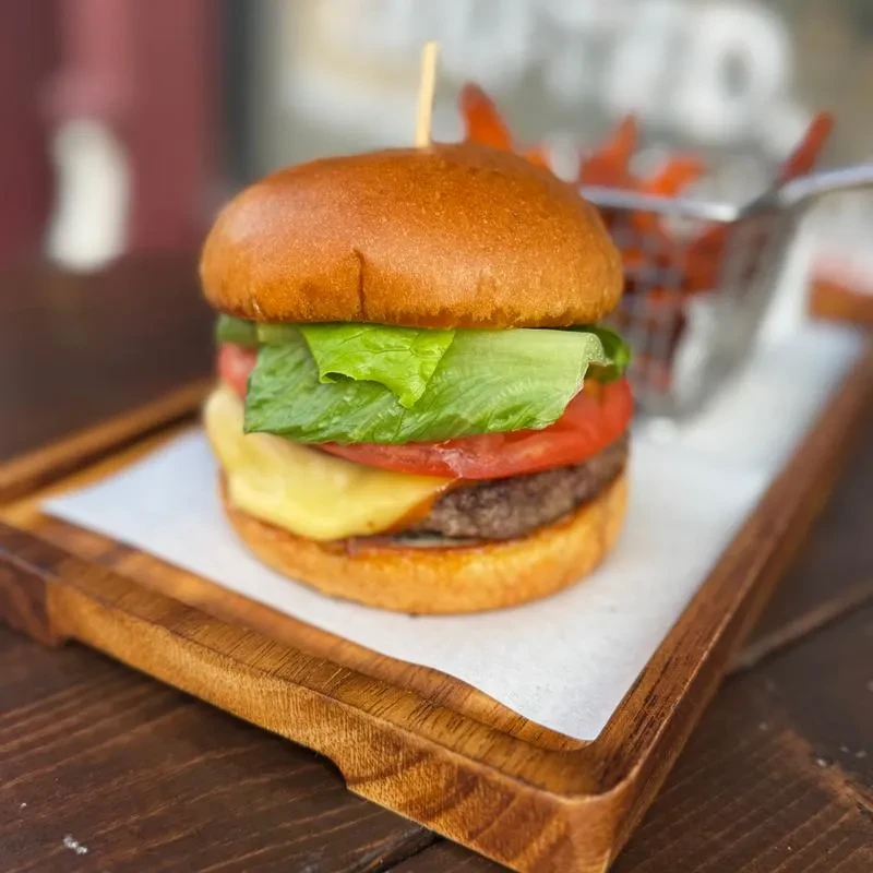 Close-up of a beef burger with cheese, tomato, lettuce, and fries.