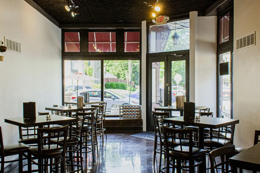 Modern restaurant interior with dark high-top seating, white walls, street view.