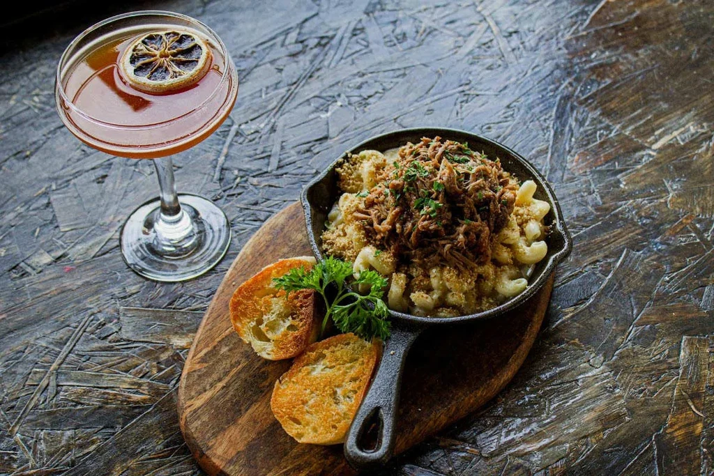 Skillet mac and cheese with shredded meat, bread, and an amber cocktail.