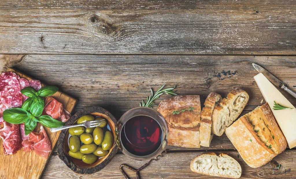 Top-down: Rustic table with meats, cheese, olives, bread, red wine.