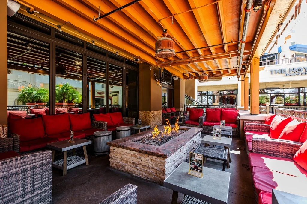 Outdoor restaurant patio with red wicker seating around an active fire pit.