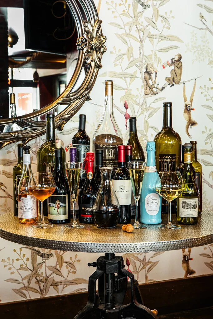 Wine and liquor bottles, glasses on metal table, monkey wallpaper, gilded mirror.