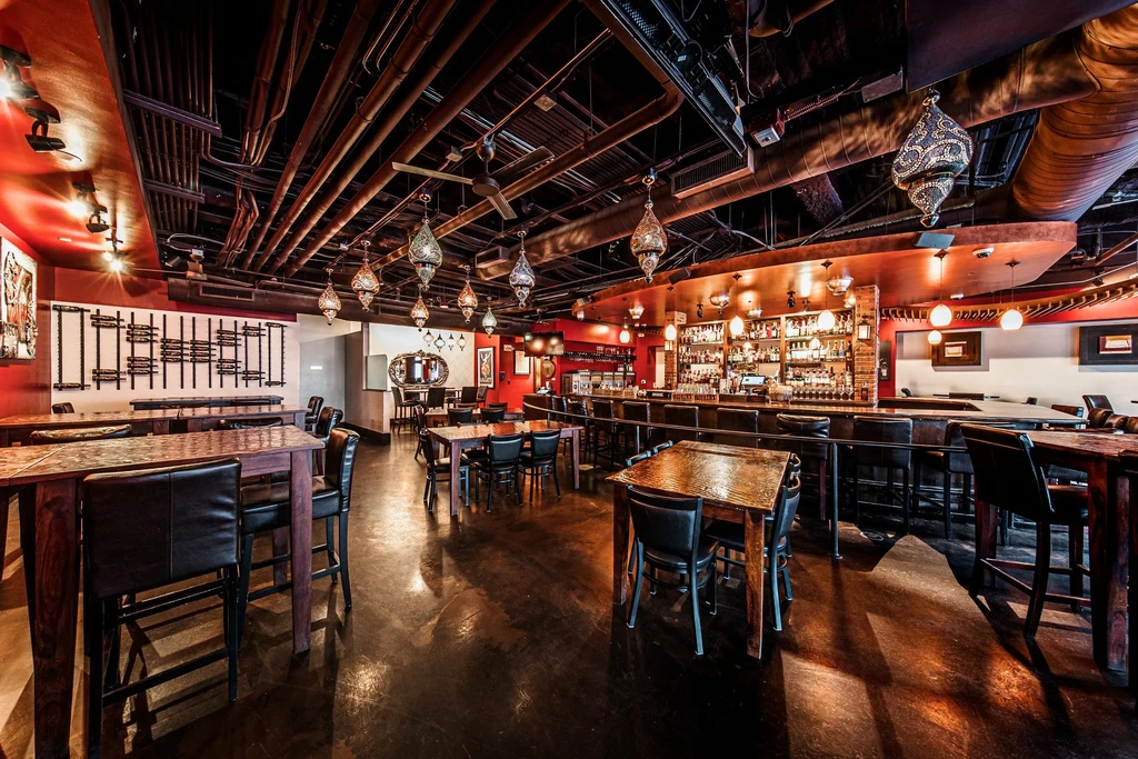 Empty restaurant bar with industrial ceiling, red walls, and ornate lanterns.