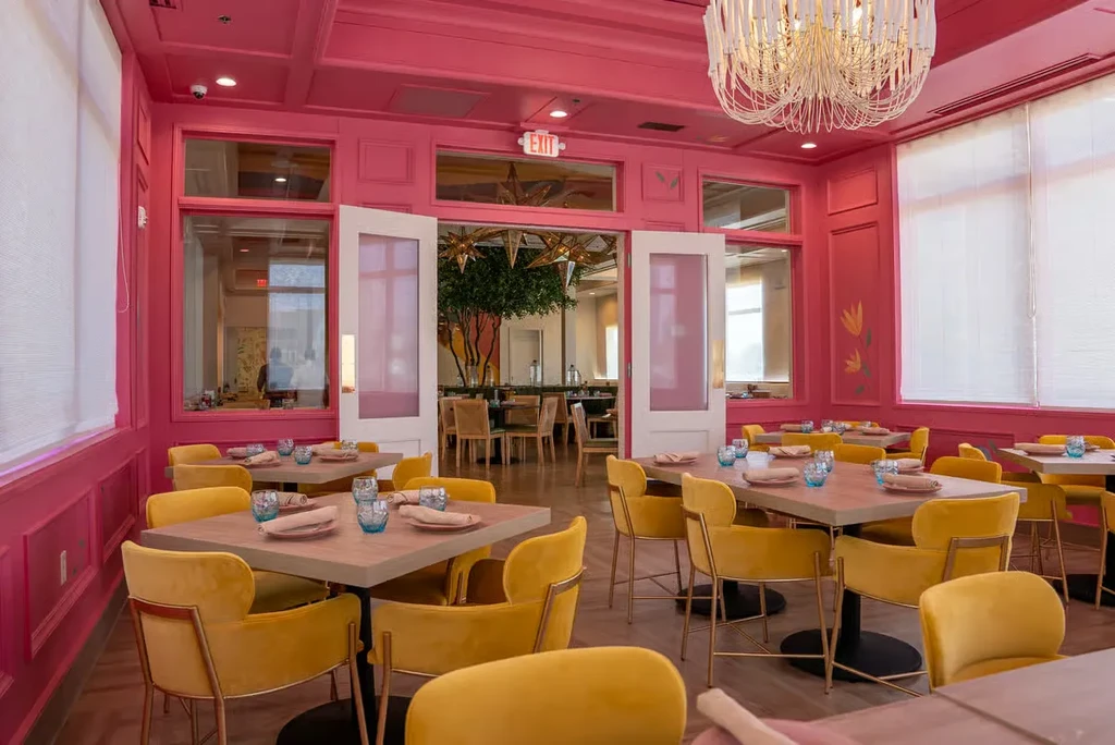 Bright pink restaurant dining room with yellow chairs and chandelier.