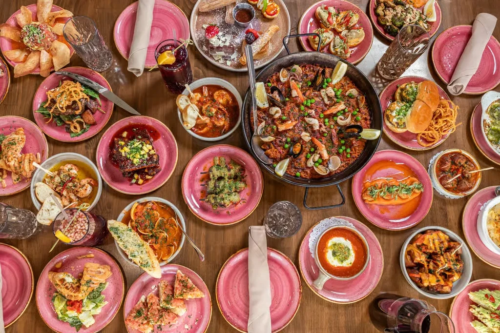 Overhead wooden table overflowing with seafood paella and diverse dishes.