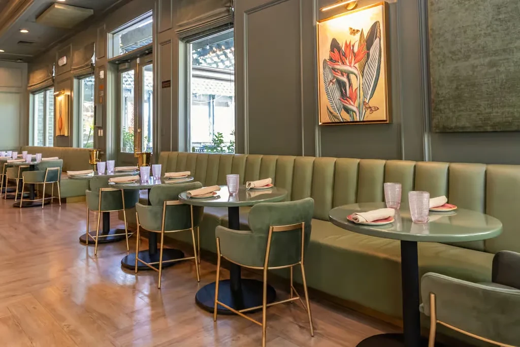 Green-themed modern restaurant with plush booths, set tables, and wall art.