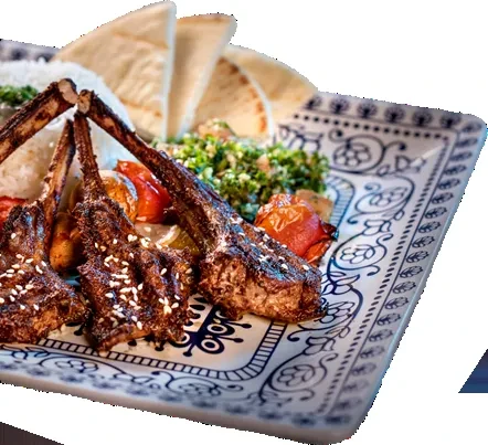 Ornate plate with seared lamb chops, rice, salad, tomatoes, and pita.