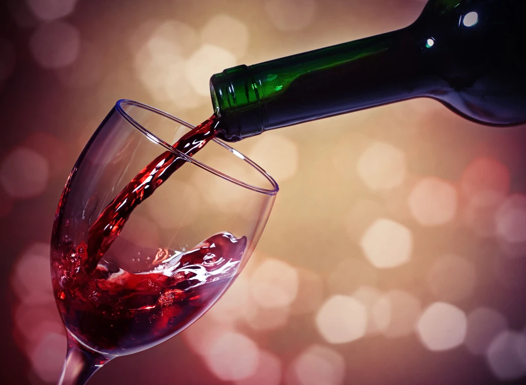 Red wine pours from a bottle into a tilted glass, splashing.