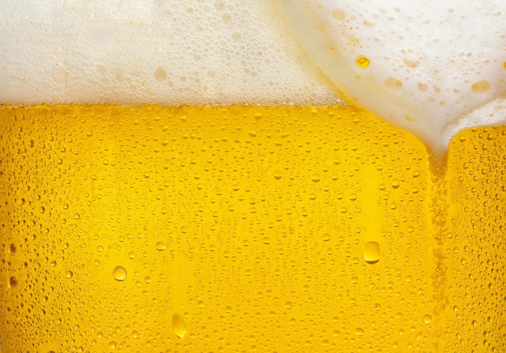 Glass of cold golden beer with thick foam and condensation.