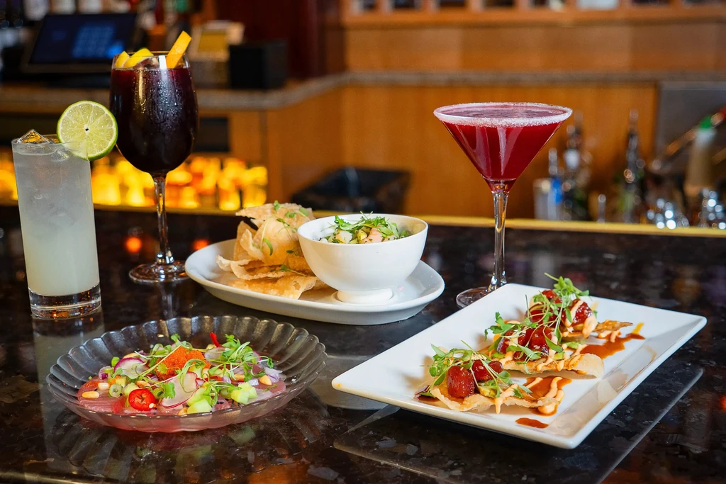 Vibrant display of cocktails, ceviche, poke, and salads on a bar.