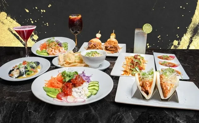 Diverse plated seafood, sliders, enchiladas, and cocktails on a dark table.