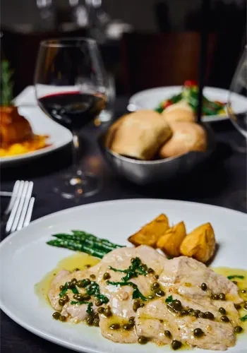 Close-up of main course with meat, capers, asparagus, potatoes, red wine.