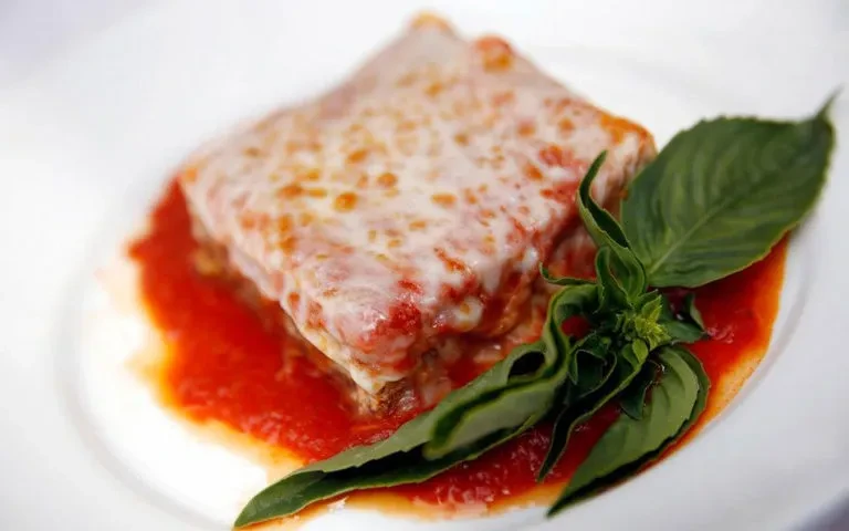 Top-down view of cheesy baked pasta with red sauce and basil.
