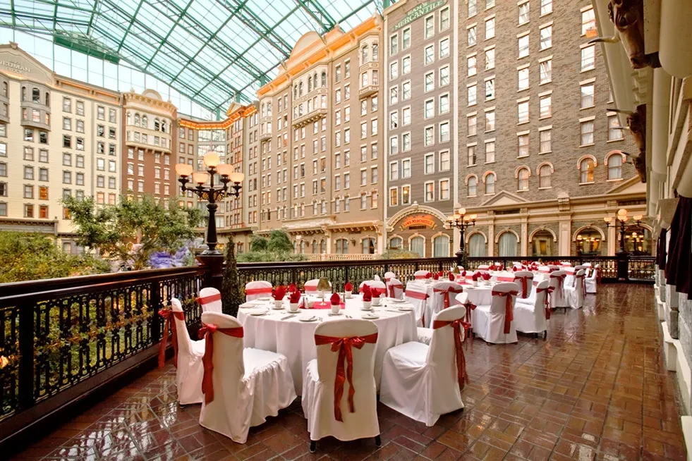 Formal dining tables in a grand glass-roofed hotel atrium.